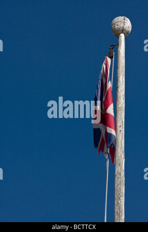 A weathered, tattered union jack dangles from a wooden flagpole Stock Photo