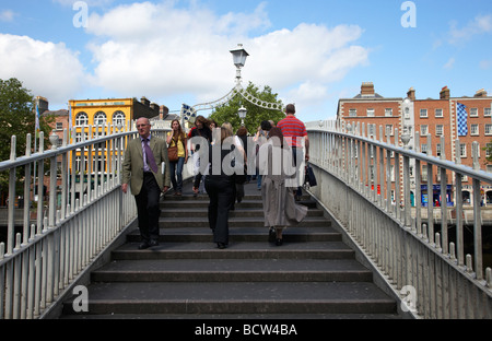 pedestrians crossing the halfpenny hapenny bridge over the river liffey in the centre of dublin city republic of ireland Stock Photo