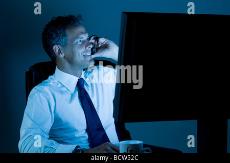 Mature businessman working till late in the night in his office and talking on mobile Stock Photo