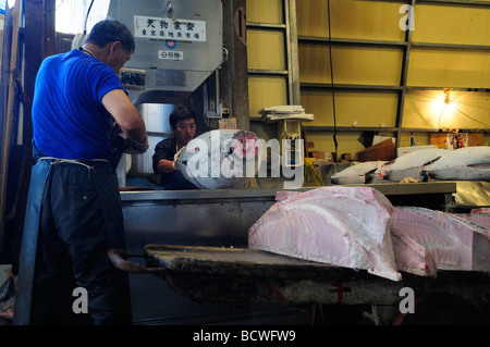 Workers cutting frozen tuna at Tsukiji world's largest fish market Central Tokyo Japan Stock Photo