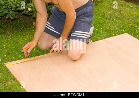 Handyman Measuring a Sheet of Wood With a Tape Measure Stock Photo