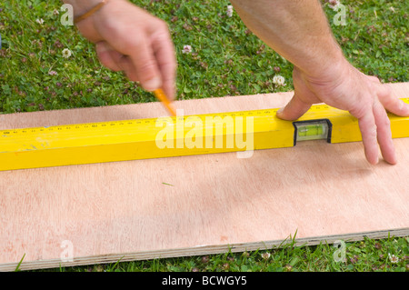 Handyman Marking a Straight Line On a Sheet Of Wood Using a Spirit Level Stock Photo