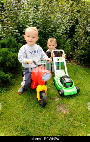 Young little children 2 3 4   years  boys playing mower on garden Stock Photo