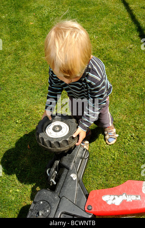 Child blond Boy playing - repairing a toy plastic tractor Stock Photo