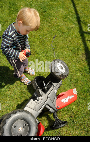 Child blond Boy playing - repairing a toy plastic tractor Stock Photo