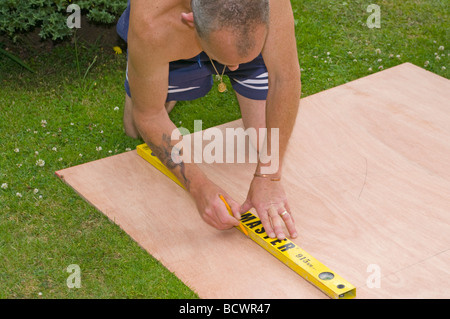 Handyman Marking a Straight Line On a Sheet Of Wood Using a Spirit Level Stock Photo