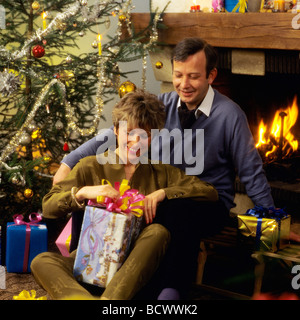 MR COUPLE EXCHANGING CHRISTMAS PRESENTS BY FIREPLACE Stock Photo