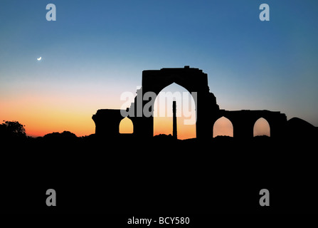 The silhouette of the famous Iron Pillar,  located in the ruins surrounding the Qutb Minar minaret, is highlighted at sunset. Stock Photo
