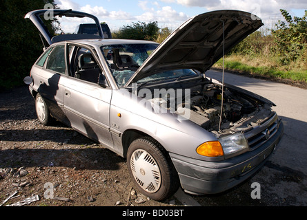 An stolen Vauxhall Astra car abandoned on a country lane with windows smashed and bonnet opened. Stock Photo