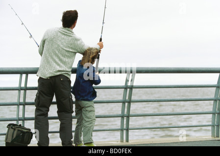 Father and son fishing from pier, father helping son with his fishing rod Stock Photo