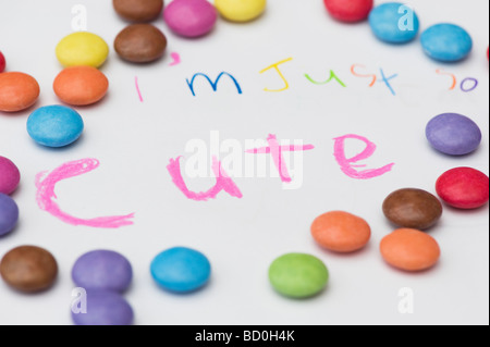 Childs spelling 'im so cute' and smarties on white Stock Photo