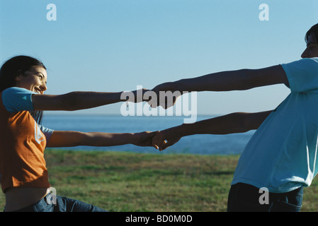 Young couple facing one another holding hands and leaning back smiling Stock Photo