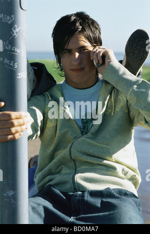 Teenage boy using cell phone, friend's feet resting on his shoulders Stock Photo