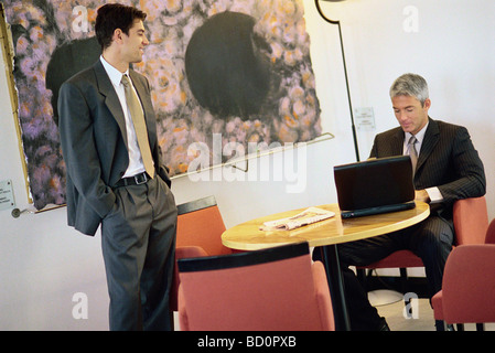 Businessmen chatting in break room, one using laptop computer Stock Photo