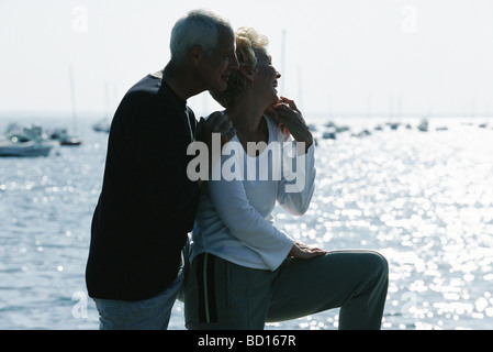 Mature couple standing together on pier, looking at view, backlit Stock Photo