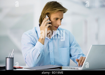 Man working at desk, using cell phone and laptop computer Stock Photo