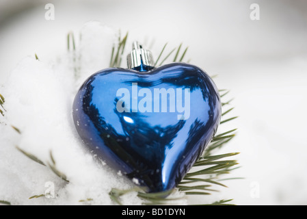 Heart shaped Christmas ornament on snow-covered evergreen branch Stock Photo