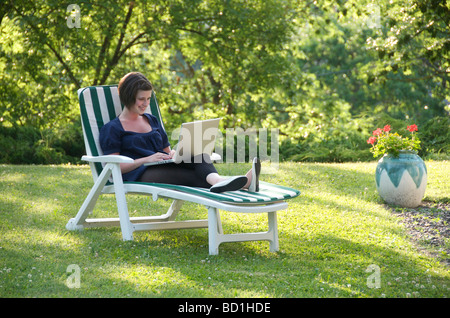 Young girl student working / revising on a laptop computer sitting on a chair in the garden. Stock Photo