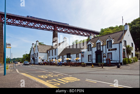 Famous Hawes Inn in South Queensferry Scotland with a First Scotrail DMU passes above on the Firth of Forth Rail Bridge Stock Photo