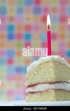 Slice of birthday cake with a lighted candle against a colourful pastel background