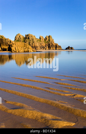 reflections at sunset Pednvounder beach near porthcurno with Logan Rock in distance cornwall Stock Photo