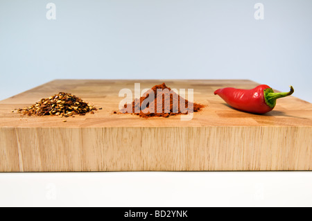 Selection of chilli types, dried, powdered and fresh, on wooden chopping board Stock Photo