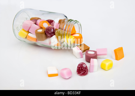 Close up of dolly mixture sweets tumbling out of glass jar against a white background Stock Photo