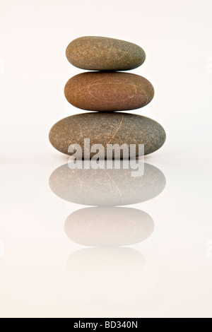 Still life shot of three beach pebbles balanced in a stone pile against white background with reflection Stock Photo