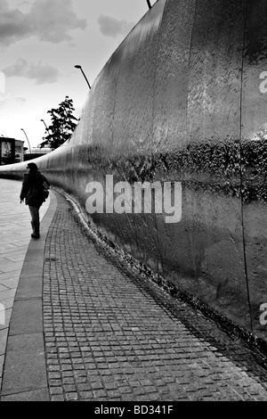 A young woman walking alongside the water cascade in Sheaf Square, outside the train station in Sheffield. Stock Photo