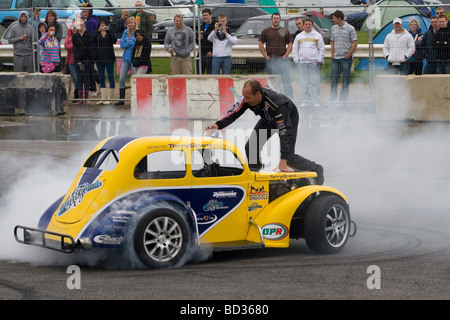 Terry Grant stuntman climbs out of his car whilst performing a stunt as part of his show at Santa Pod Stock Photo