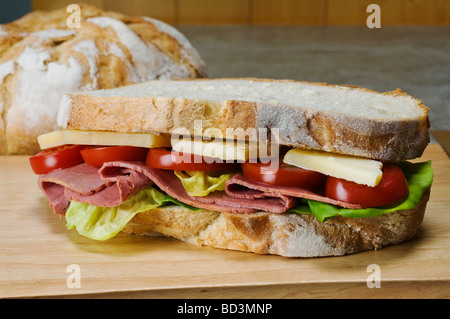 A sandwich of  french boule white bread with a filling of lettuce pastrami cheddar cheese and tomato slices Stock Photo