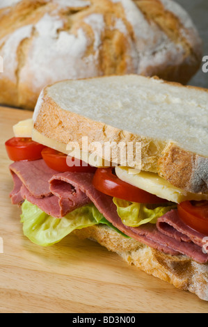 A sandwich of  french boule white bread with a filling of lettuce pastrami cheddar cheese and tomato slices Stock Photo