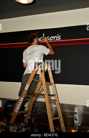 Sign painter on ladder painting new meat store name logo on wall Stock Photo