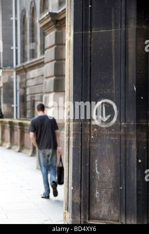 A pillar on Teviot Place, Edinburgh with some graffiti and circle with a downwards arrow. A man walks past in the background Stock Photo