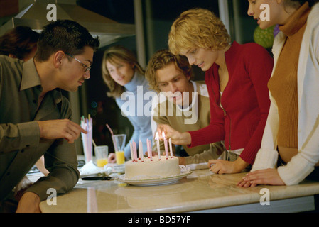 Woman lighting candles on birthday cake, others standing by watching Stock Photo