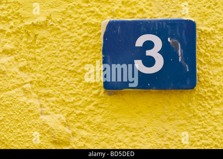 Blue ceramic tile indicating street number 3 on the yellow wall of a building in Deira, Dubai, United Arab Emirates (UAE) Stock Photo