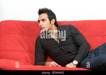 Young man sat on red sofa Stock Photo