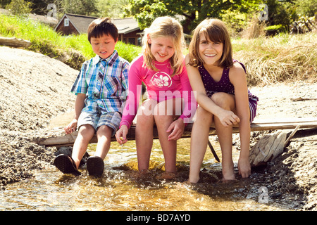Children sitting on log bridge above creek