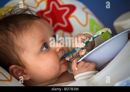 Young baby under six months old spoon feeding and making a mess Stock Photo