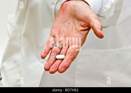 A woman in a doctors smock holding single white pill in her hand Stock Photo
