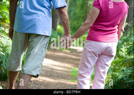mature couple holding hands, walking on woodland track, norfolk, england Stock Photo