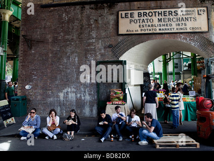 People sit and eat on pavement near Lee Brothers, Borough Market, London Stock Photo