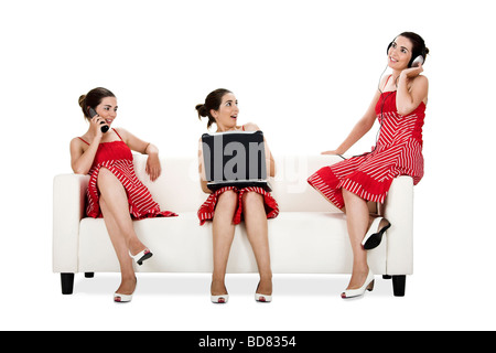 Three happy twin sisters seated on a couch doing different activities Picture collage of the same woman in different poses Stock Photo