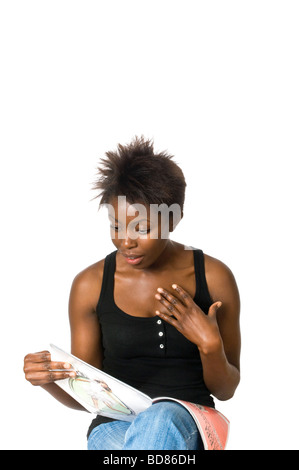Vertical close up portrait of an attractive African woman looking shocked whilst reading a fashion magazine Stock Photo