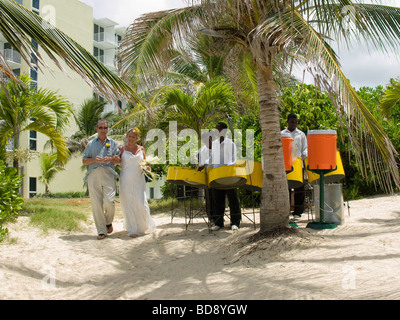 A smiling bride and her father walk past a steel drum band down to the beach for her wedding Stock Photo