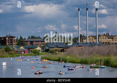 Many people leisurely floating on rafts down the Deschutes River, stacks of Old Mill district behind, July 4th, Bend Oregon Stock Photo