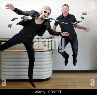 a man and woman wearing black frozen in mid air jumping in a room with a shiny wooden floor and a nineteen sixties bar Stock Photo