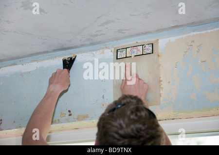 Britain UK Young man scraping wallpaper off a wall using a scraper and steamer Stock Photo