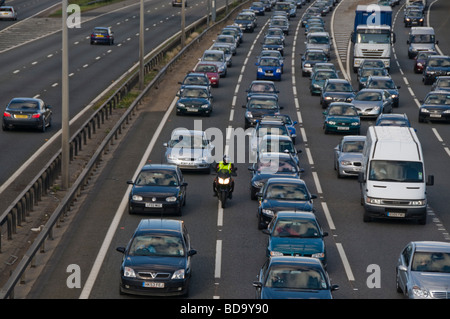 Motorcycle rides between slow moving traffic out of London at a junction on the M4 motorway Stock Photo