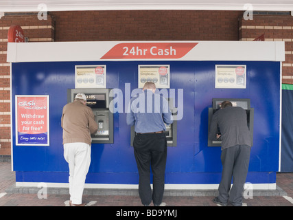 Three men withdrawing money at twenty four hour cash machine Stock Photo